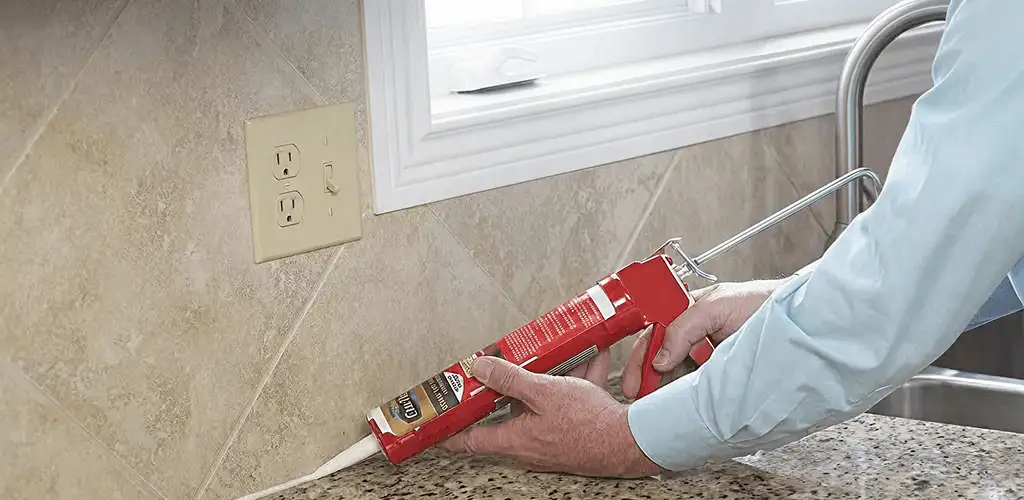 Handyman applying caulk along a kitchen backsplash and countertop seam in Detroit, MI