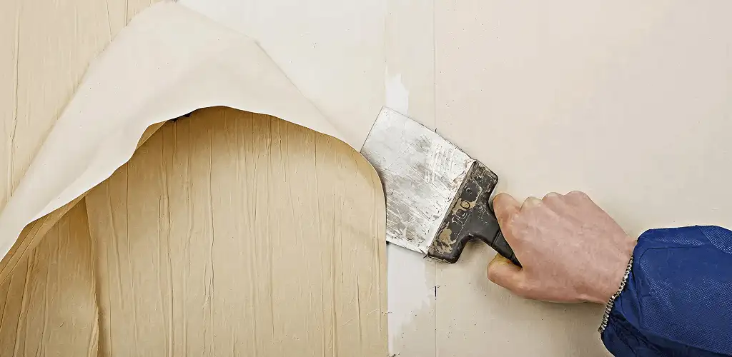 Handyman removing wallpaper with a scraper for wall preparation in Detroit, MI